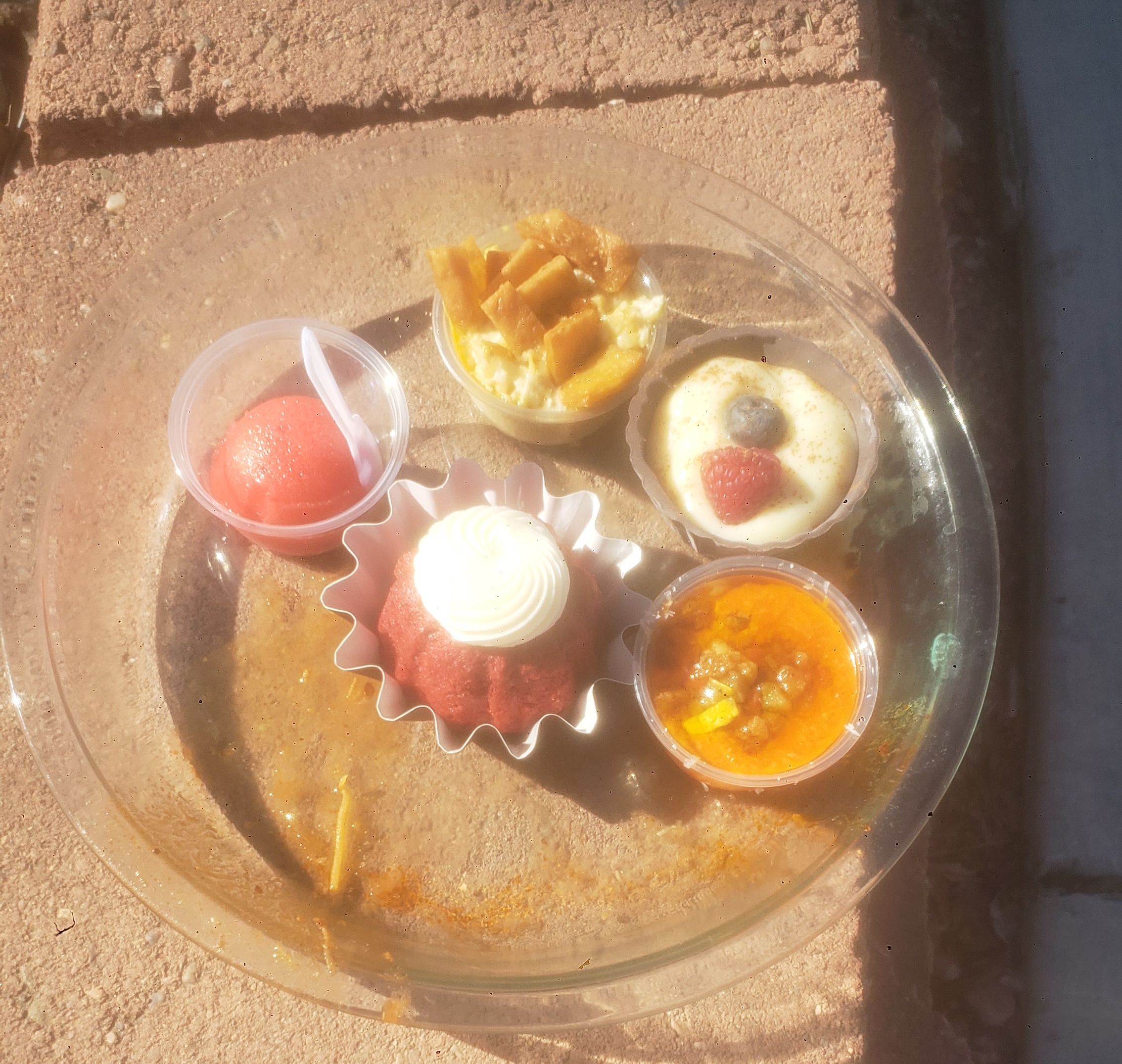 Two mini cups of soup and three mini desserts in a pie pan on a brick.